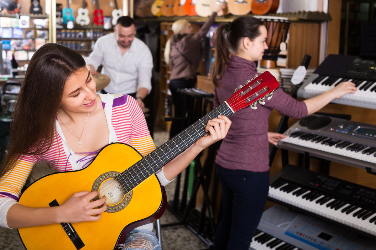 Young woman plays a yellow guitar in a music store while others browse keyboards and ukuleles.